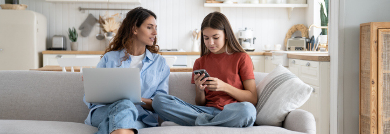 Bilde av en mor og en datter som sitter i sofaen med en PC og en mobil for å illustrere artikkelen om hvordan man velger riktig strømselskap.