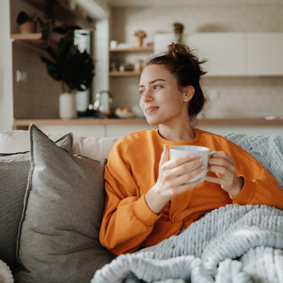 Kvinne sitter med en kopp i sofaen