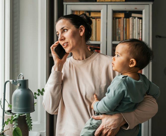 En mor snakker i telefon med en baby på armen