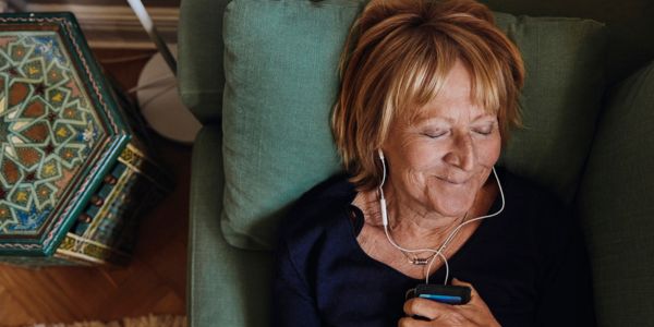Kvinne ligger på sofaen og lytter med headset til mobilen