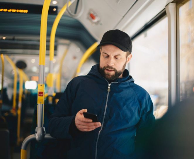 Mann sjekker mobiltelefonen på bussen