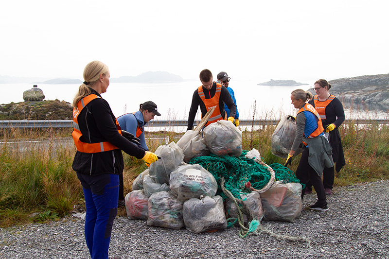 Fjordkraft-ansatte rydder en strand og viser frem fulle søppelsekker