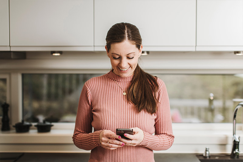 Kvinne står i hjemmet sitt og ser på Fjordkraft-appen på mobilen sin